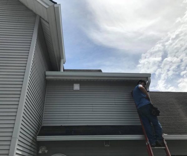 professional in blue shirt on ladder working on gutter system